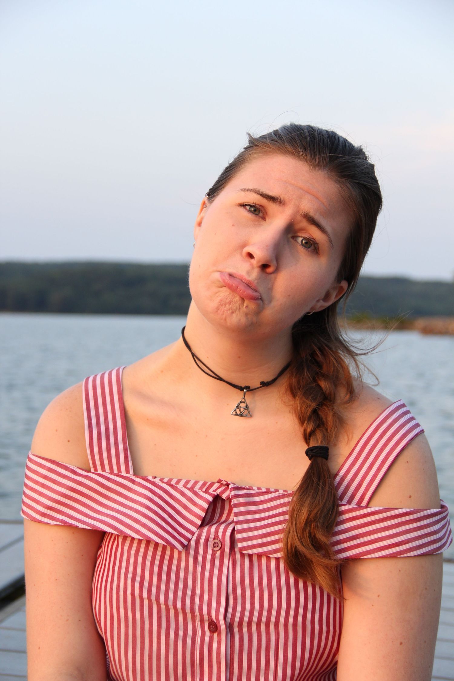 Playful expression while wearing striped top by the water at sunset.
