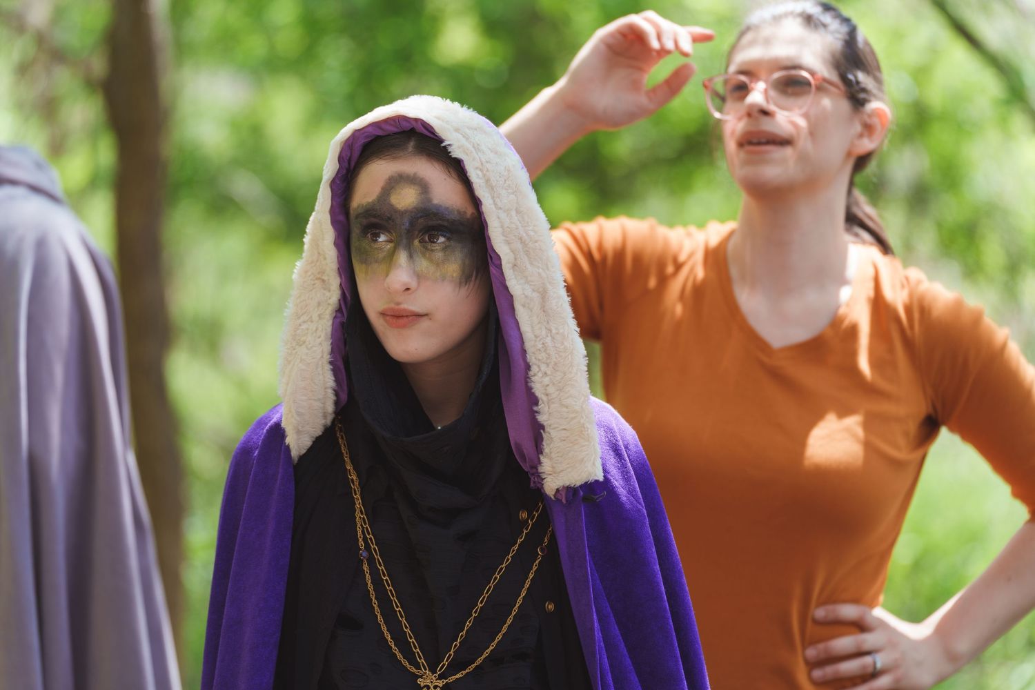 Performers in costume rehearsing scenes outdoors among trees and natural lighting.