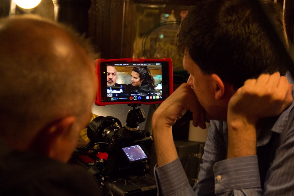 Two filmmakers review footage on a red-framed tablet monitor during an indoor video production shoot.