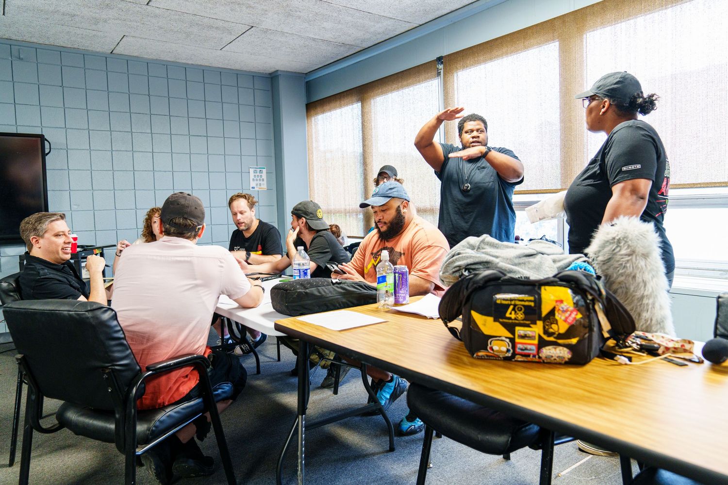 Group of workers gathered around a table in a conference room for a meeting, with tool bags and laptops visible.