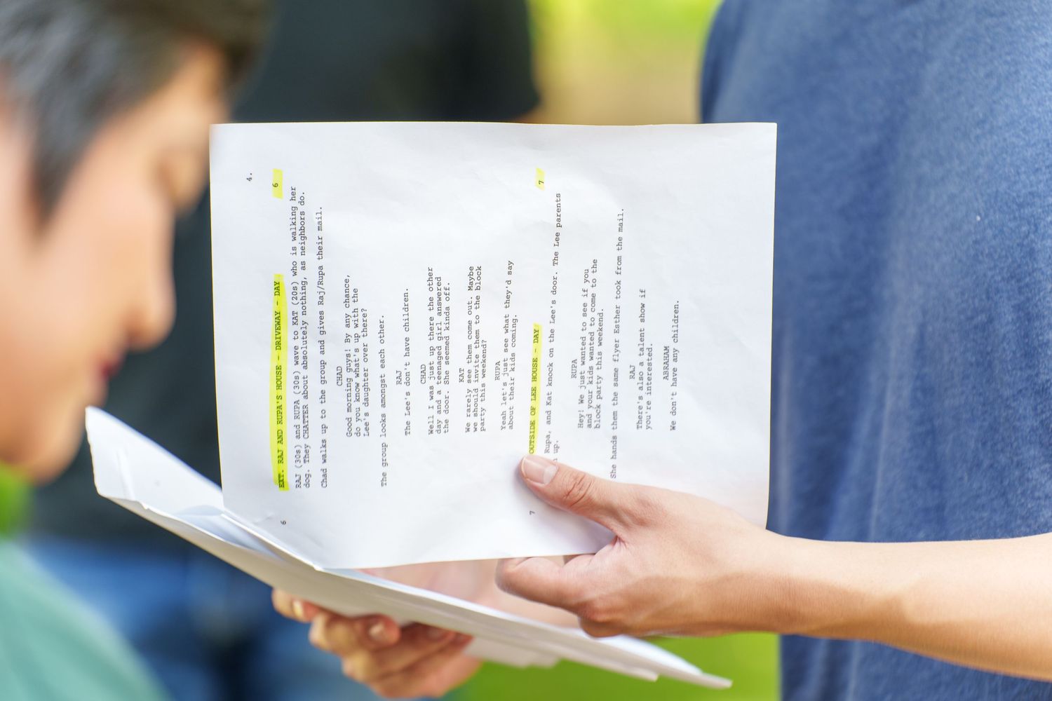 Two people reviewing highlighted script pages outdoors, holding printed documents with yellow marker annotations.