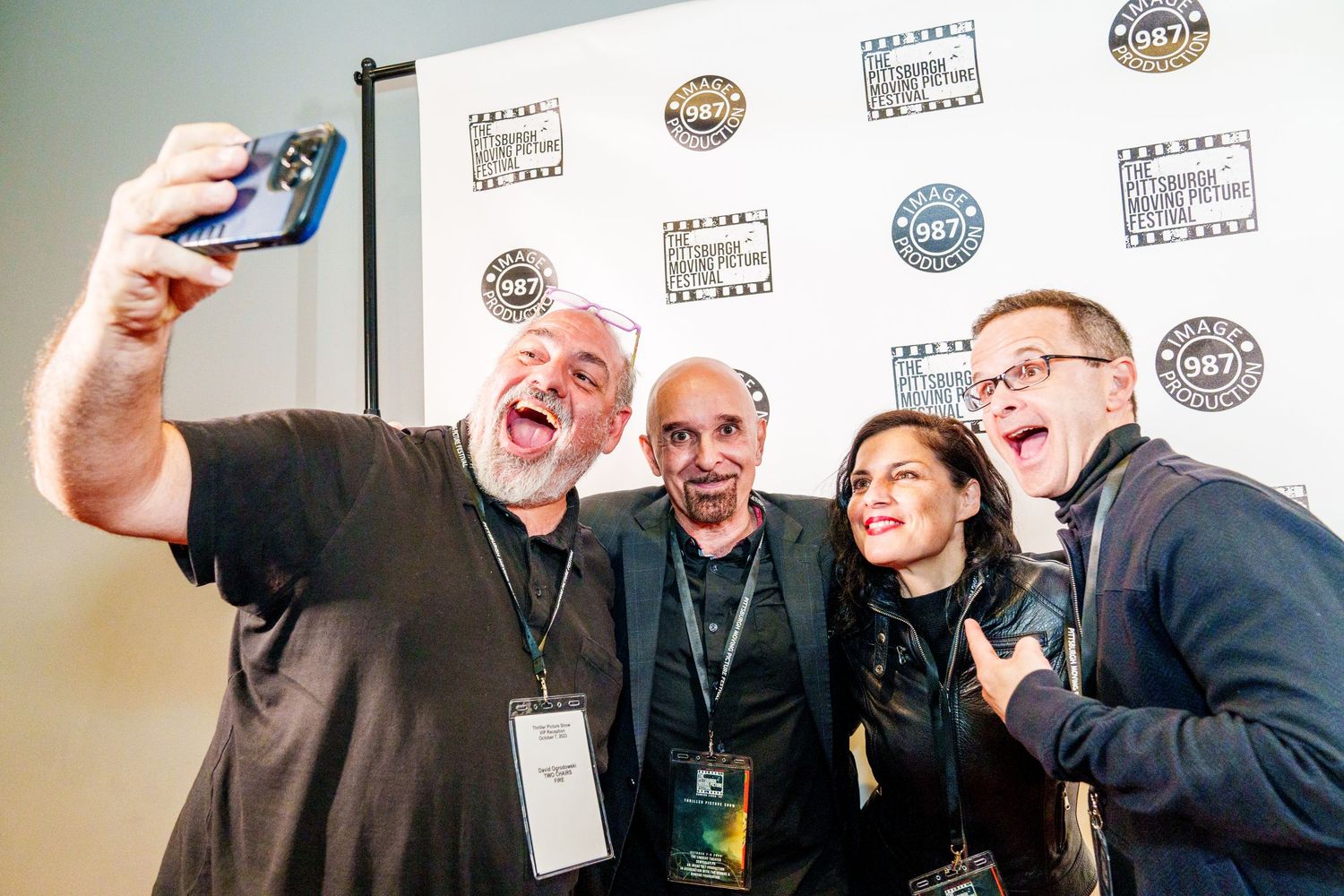 A group takes a fun selfie together while making animated expressions at an event with branded logos on the wall.