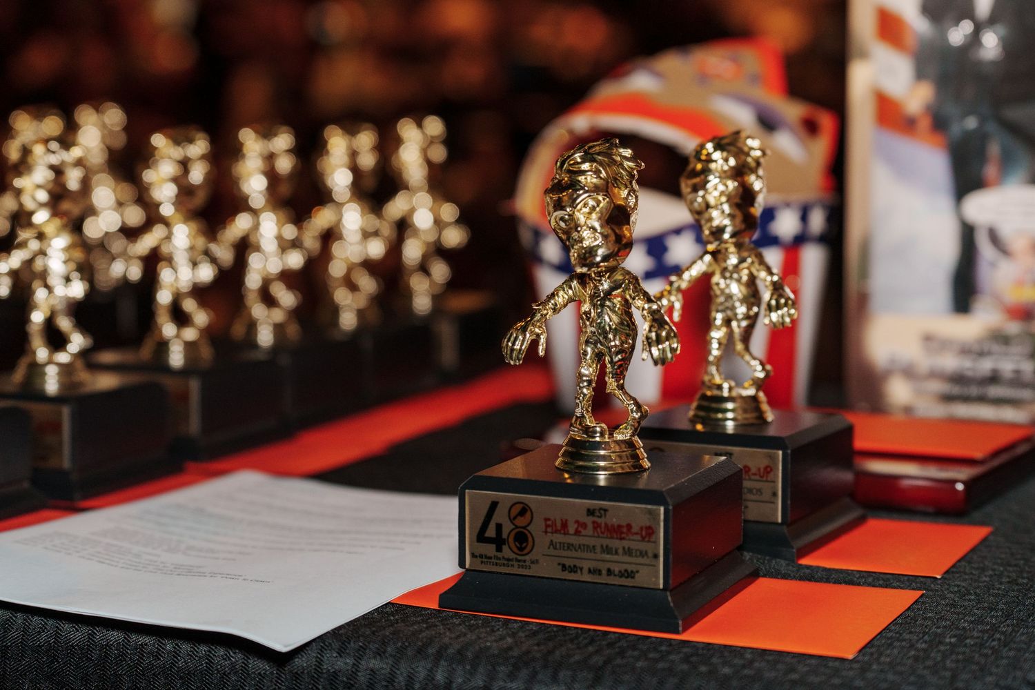 Row of golden trophy awards displayed on red and black platform at ceremony.