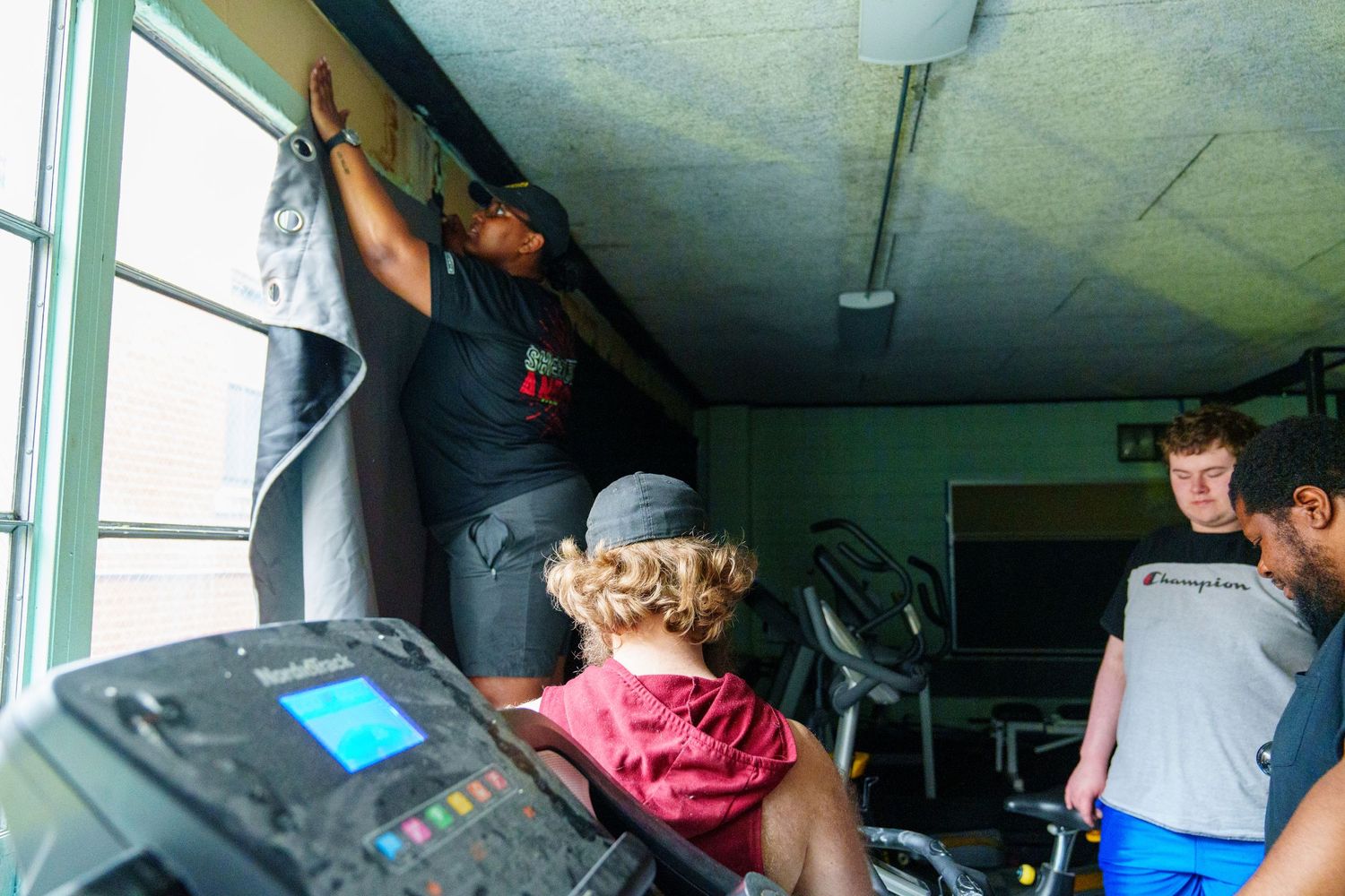 Film crew working in a small indoor space with equipment and blue exercise mats visible.