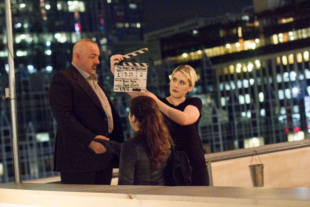 A film crew uses a clapperboard on a rooftop at night with city lights in the background.