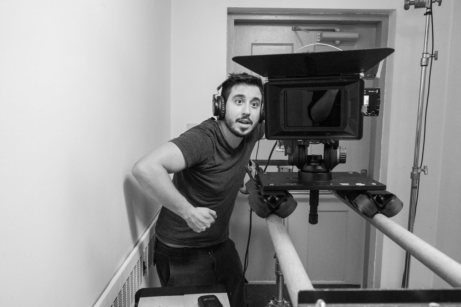 Black and white photo of a cameraman operating a film camera on a dolly track on set.