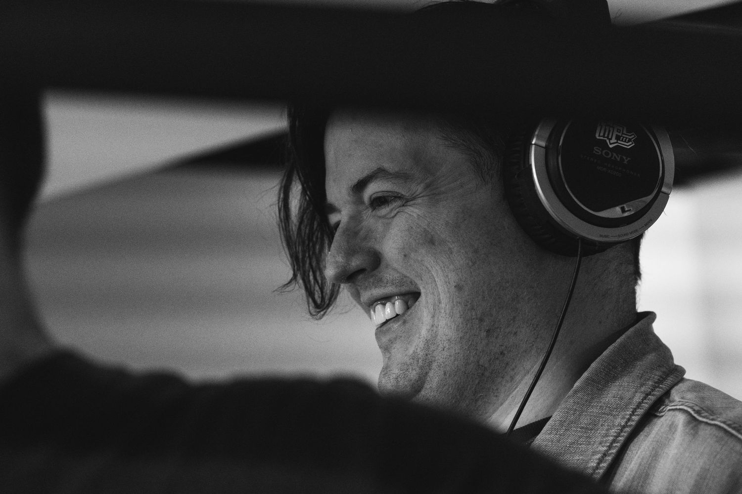Smiling man wearing headphones inside a vehicle in black and white photo.