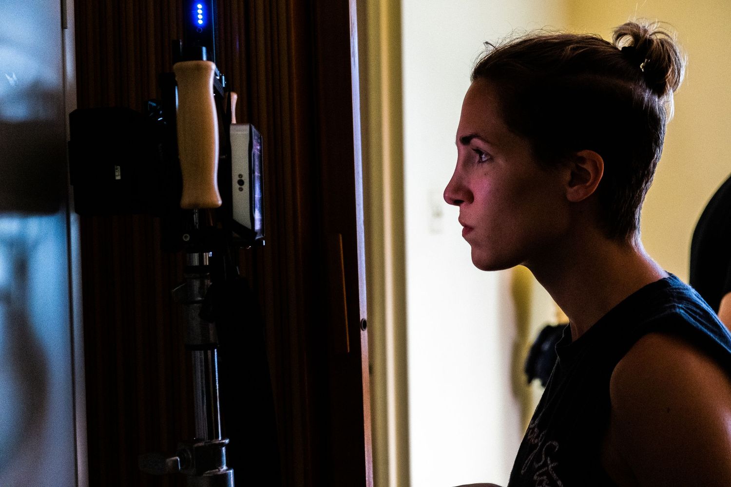 Young woman in profile view looking at a camera mounted on a tripod stand indoors.