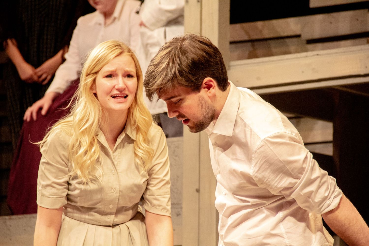 Theater scene showing performers in light colored clothing interacting on stage.