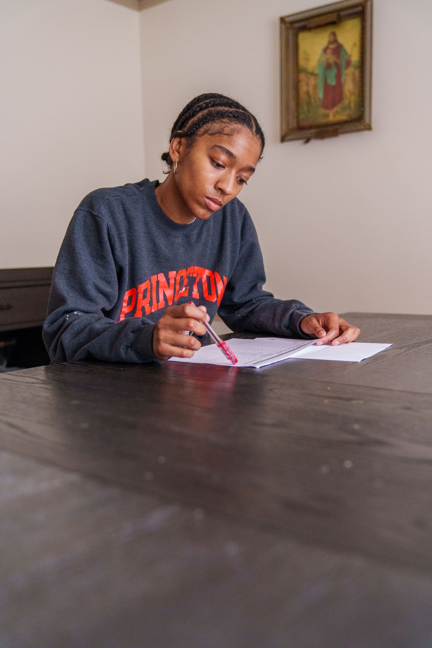 Young woman in Princeton sweatshirt writing notes at a dark wooden table with a red pen.