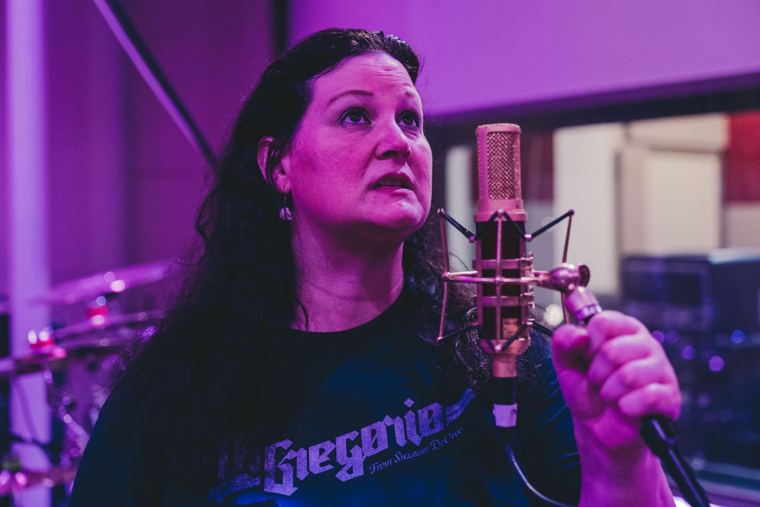 Vocalist performing in recording studio with purple lighting effects.
