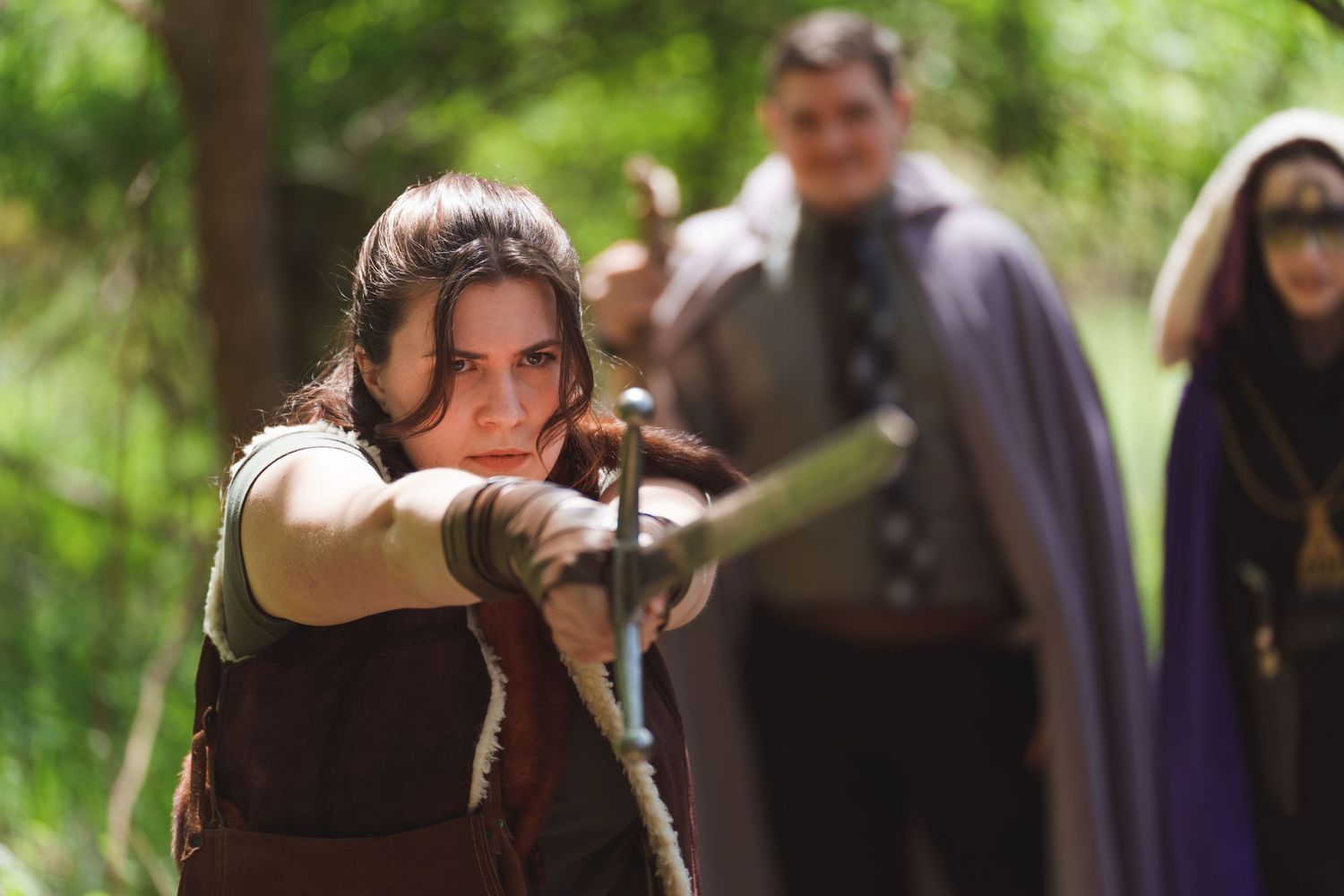 People in medieval costumes gather outdoors in a wooded area during a role-playing event.