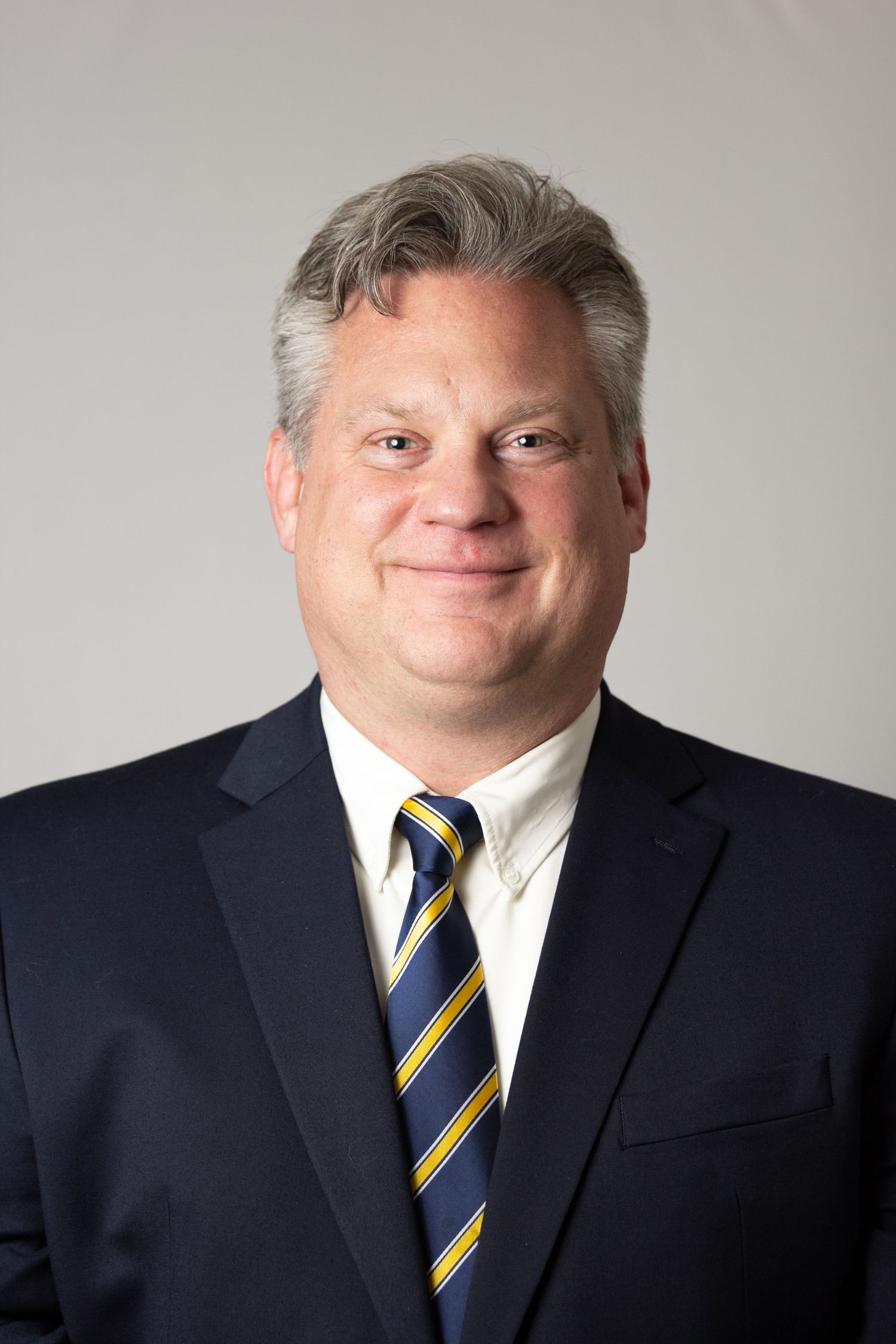 Professional headshot series showing a person in a navy suit and striped tie against a light gray background.