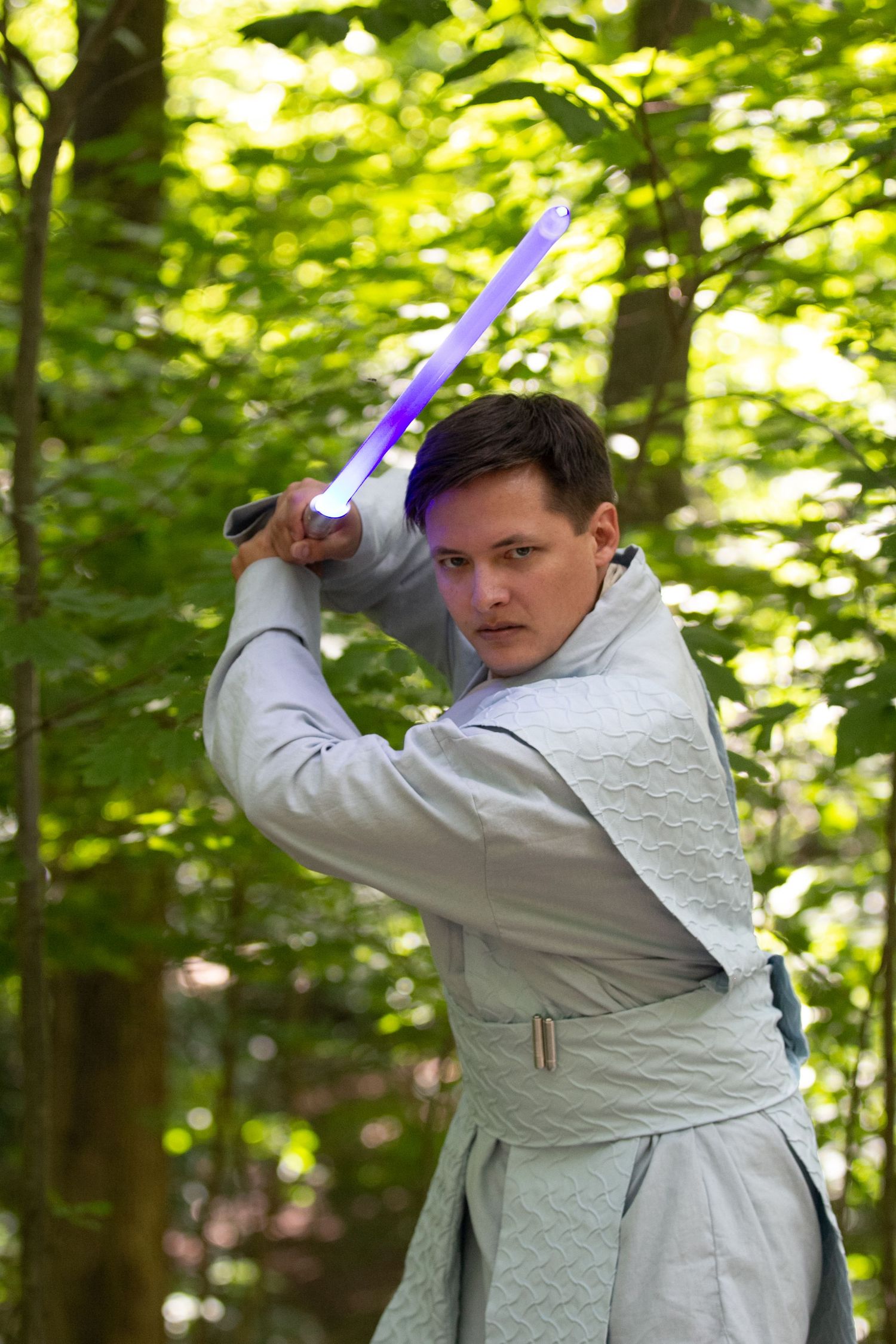 Action shots of someone in white robes performing lightsaber combat moves in a forest.