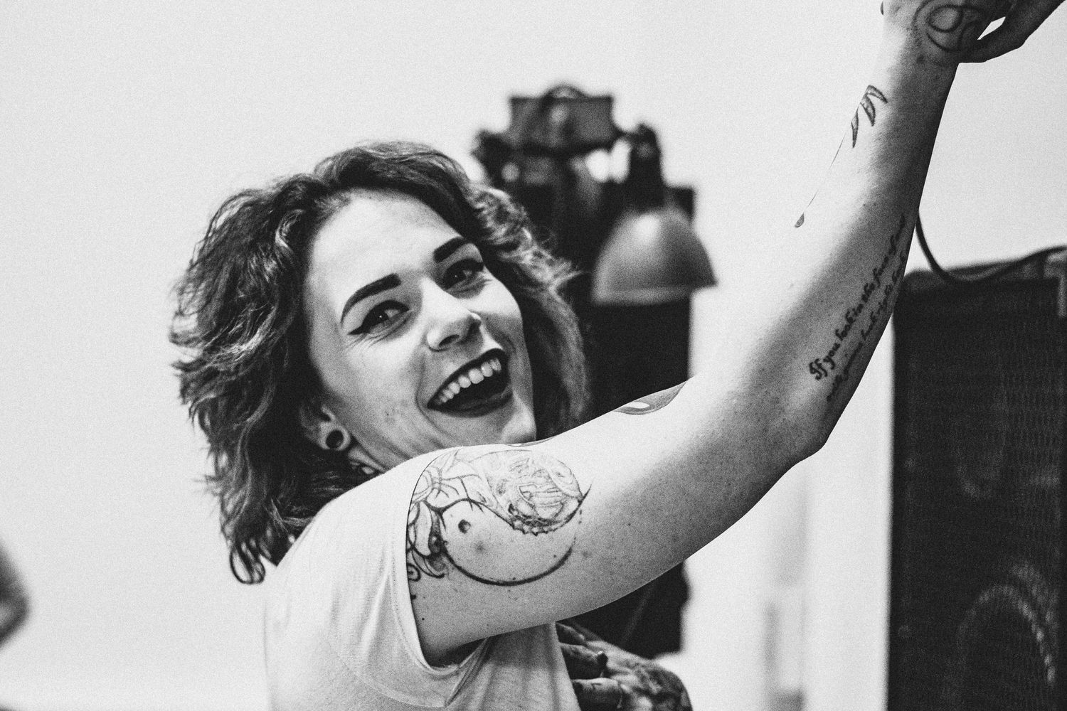 Black and white photo of a performer with visible tattoos reaching upward on stage.