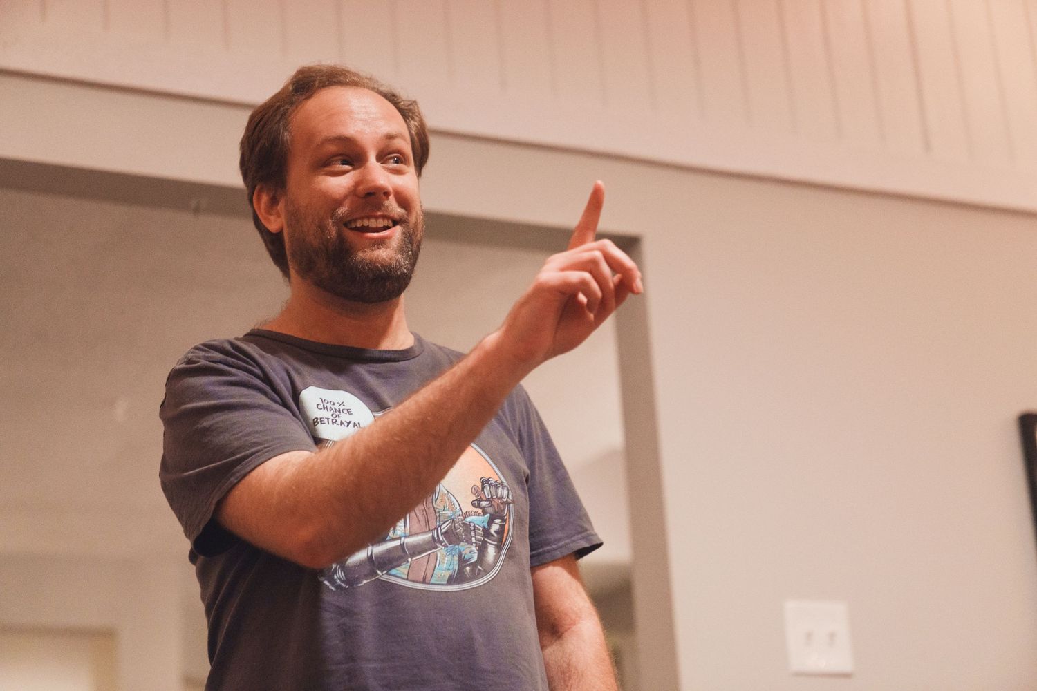 Person in gray t-shirt pointing upward with enthusiastic expression.