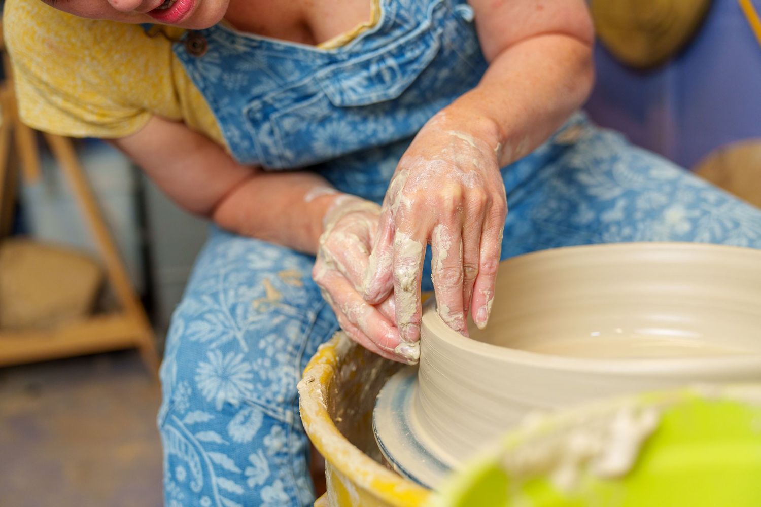 Hands work with clay on a pottery wheel, forming the rim of a ceramic piece in progress.