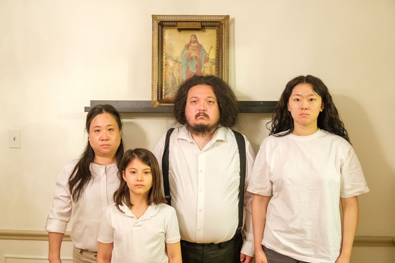 Family of four posing solemnly in front of a religious painting on a wall.