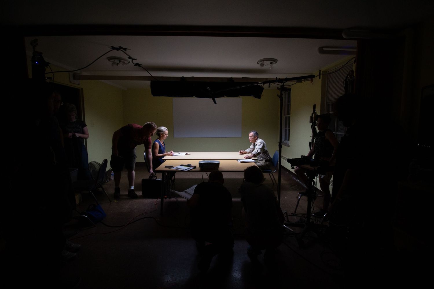 People gathered around a table in a dimly lit room with a projection screen in the background.