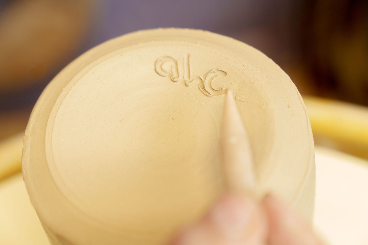 Close-up of a pottery maker carving initials into the bottom of an unfired clay ceramic bowl.