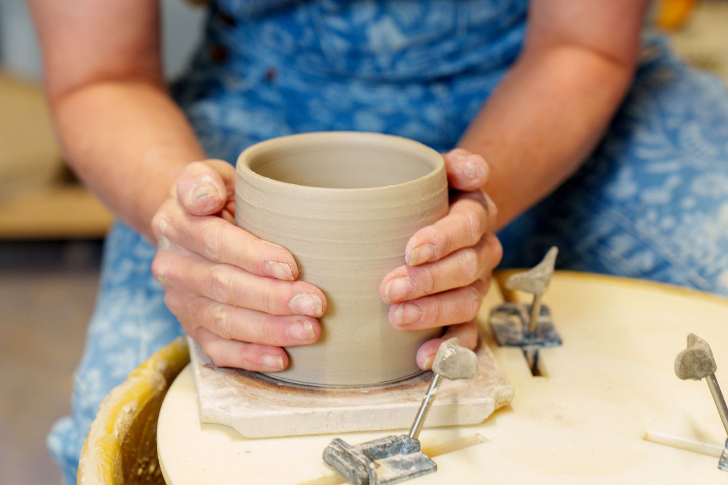 Close-up view of hands working on a pottery wheel shaping a clay bowl with blue fabric visible in background.