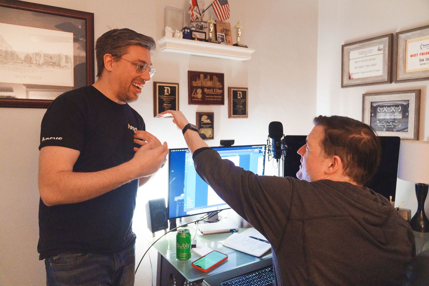 Two people high-fiving in an office with certificates on the wall.