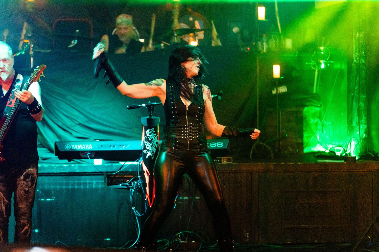 Concert stage bathed in vibrant green lighting with performers and musical equipment creating an energetic atmosphere.