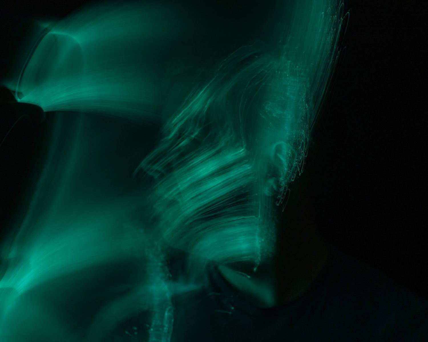 Flowing teal-colored smoke or light trails creating an ethereal pattern against darkness.