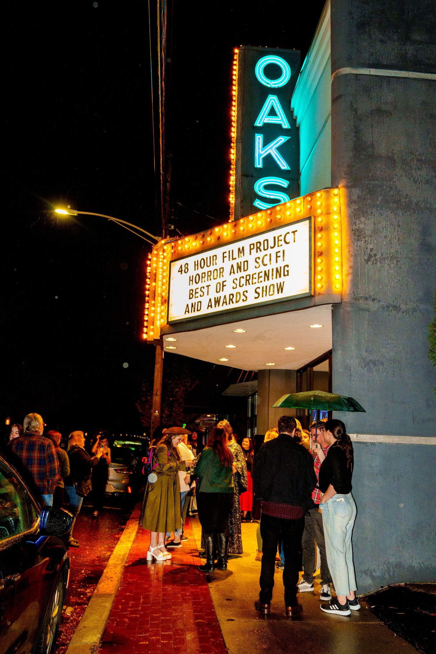 Illuminated theater marquee sign at night with people gathering outside.