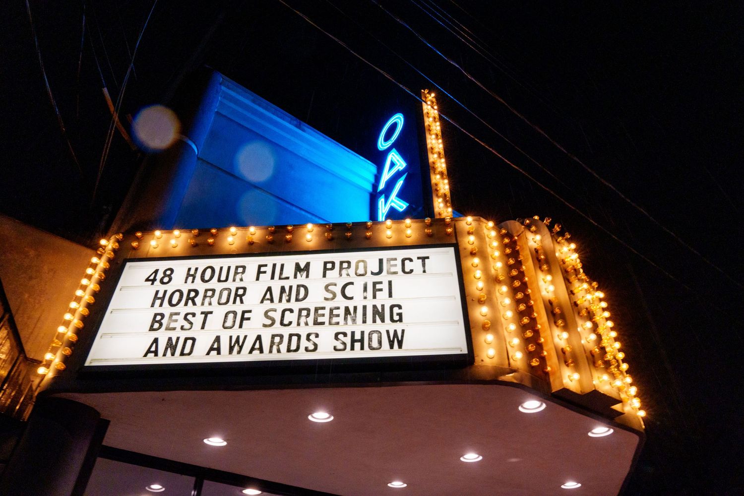 Illuminated theater marquee displaying film festival screening information at night.