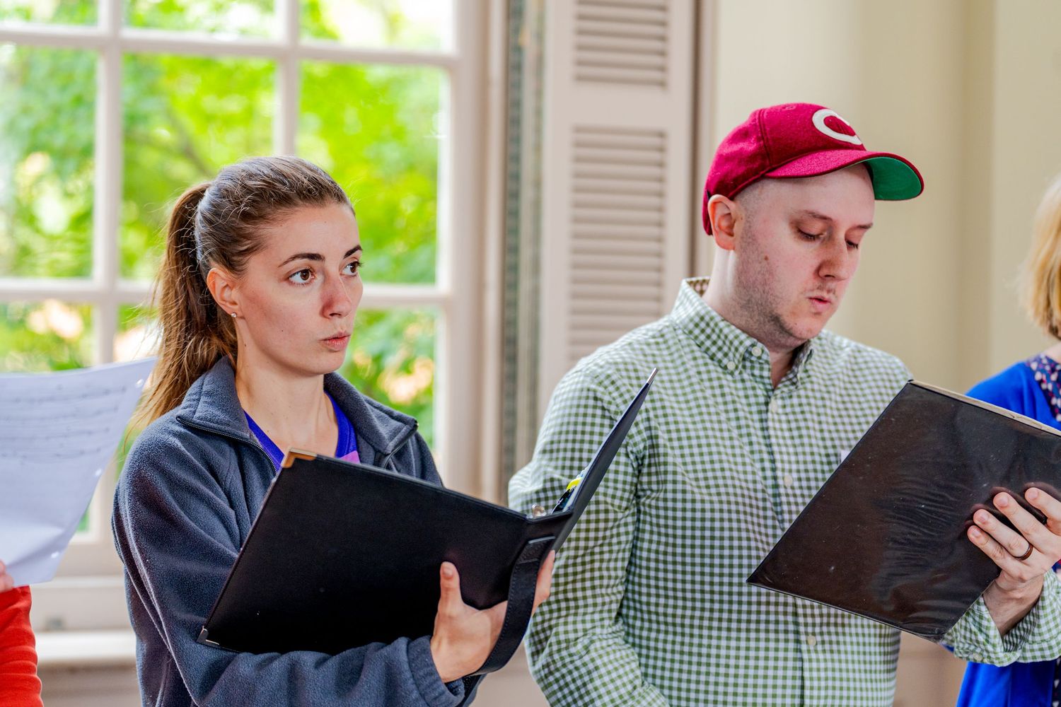 Two students reading from binders during a rehearsal or academic exercise indoors.