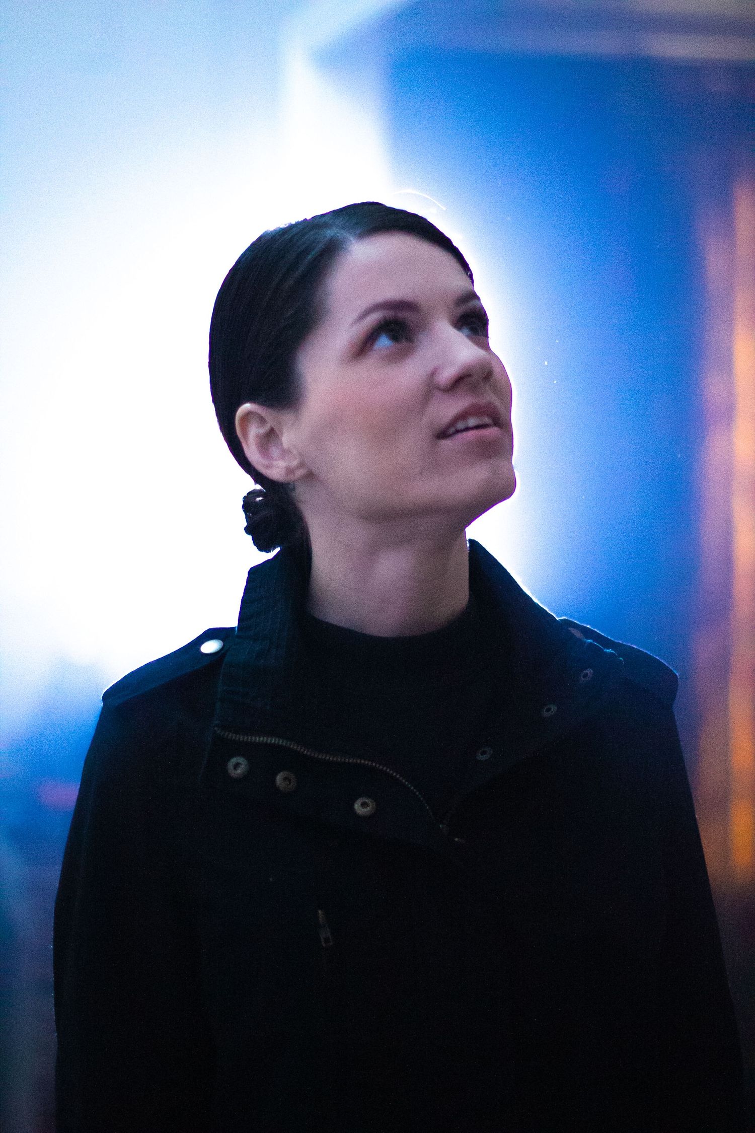 Woman in black jacket gazing upward with blue and gold bokeh lights in the background.