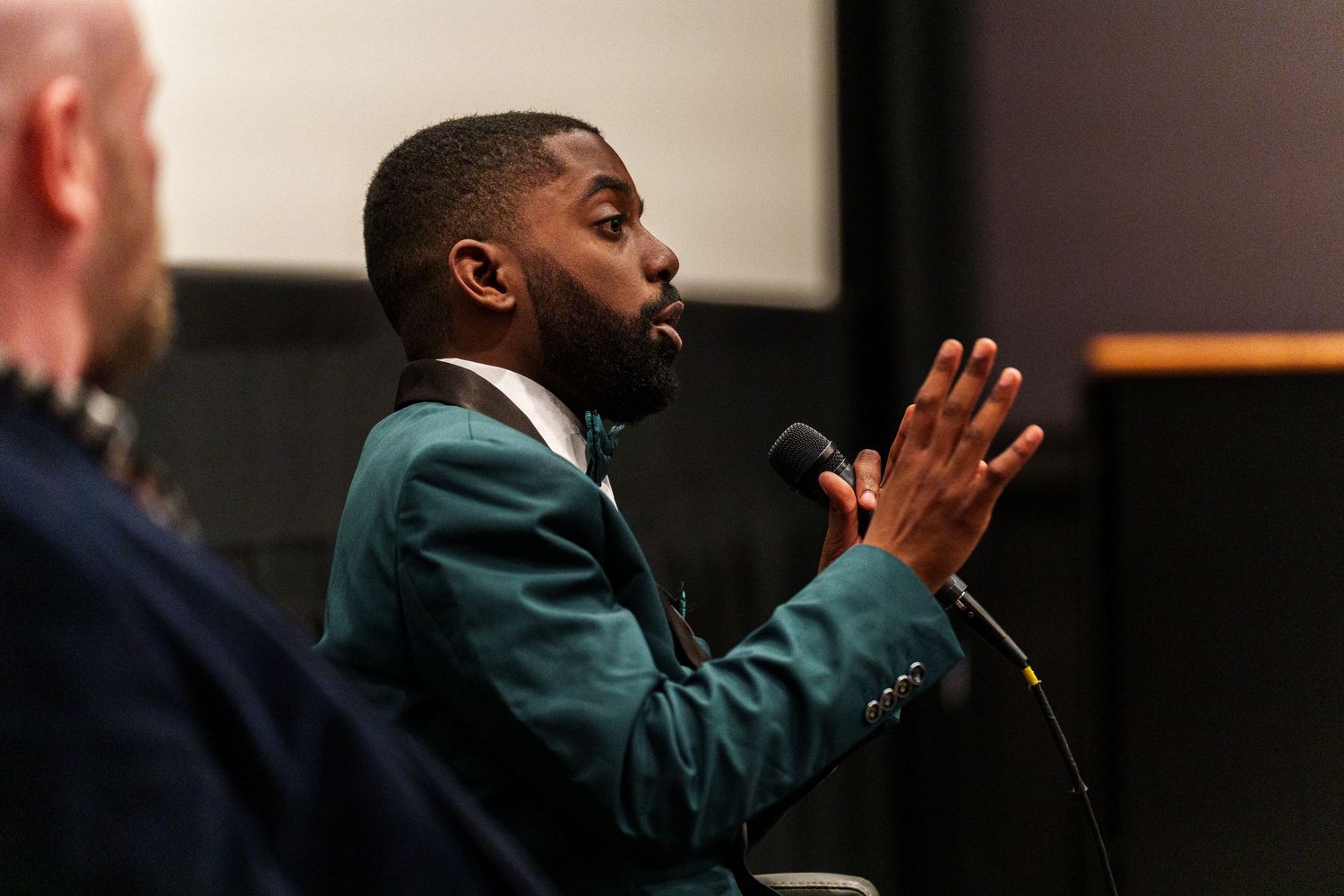 Speaker in dark suit gesturing passionately during presentation.