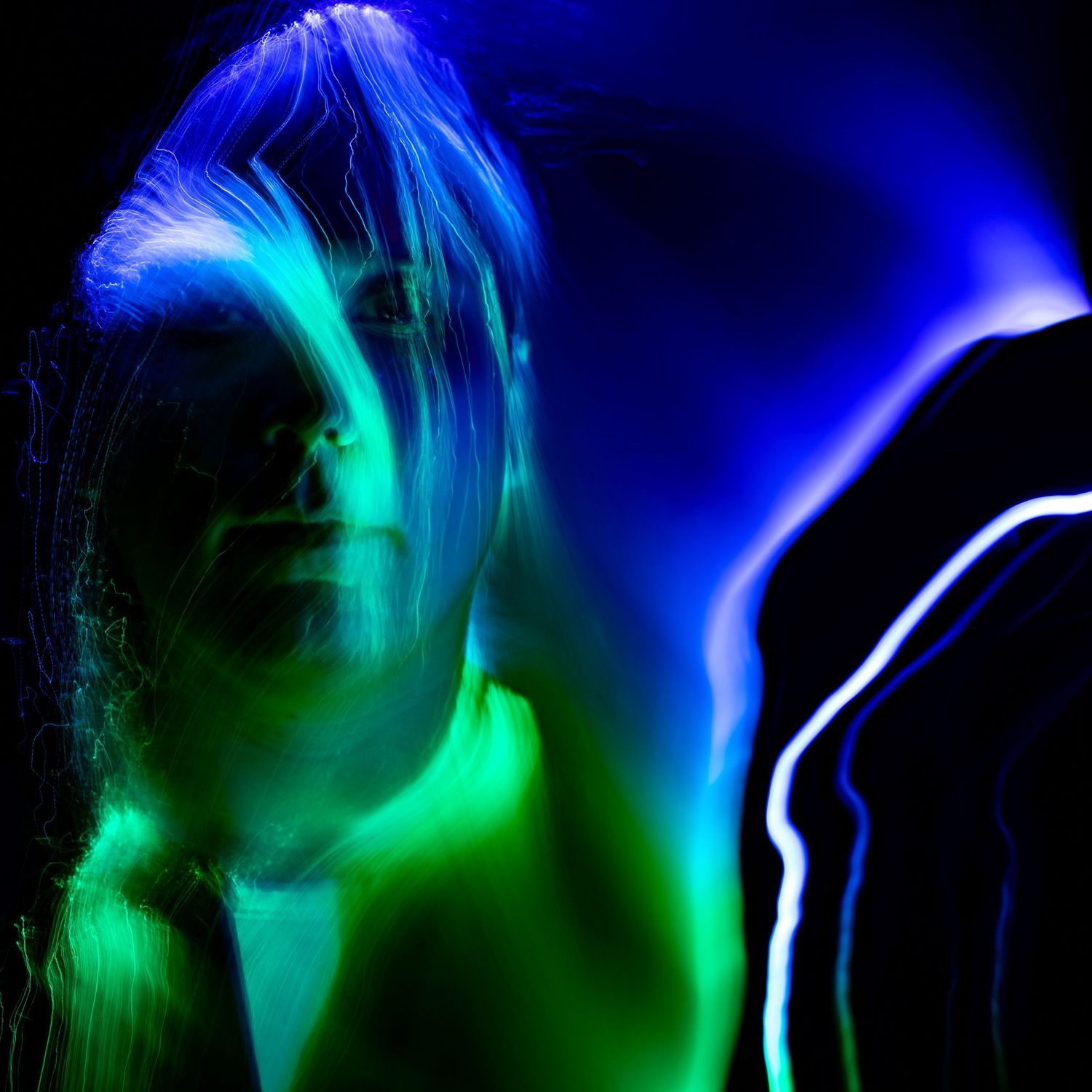 Vibrant blue and green light streaks creating an abstract pattern in darkness.