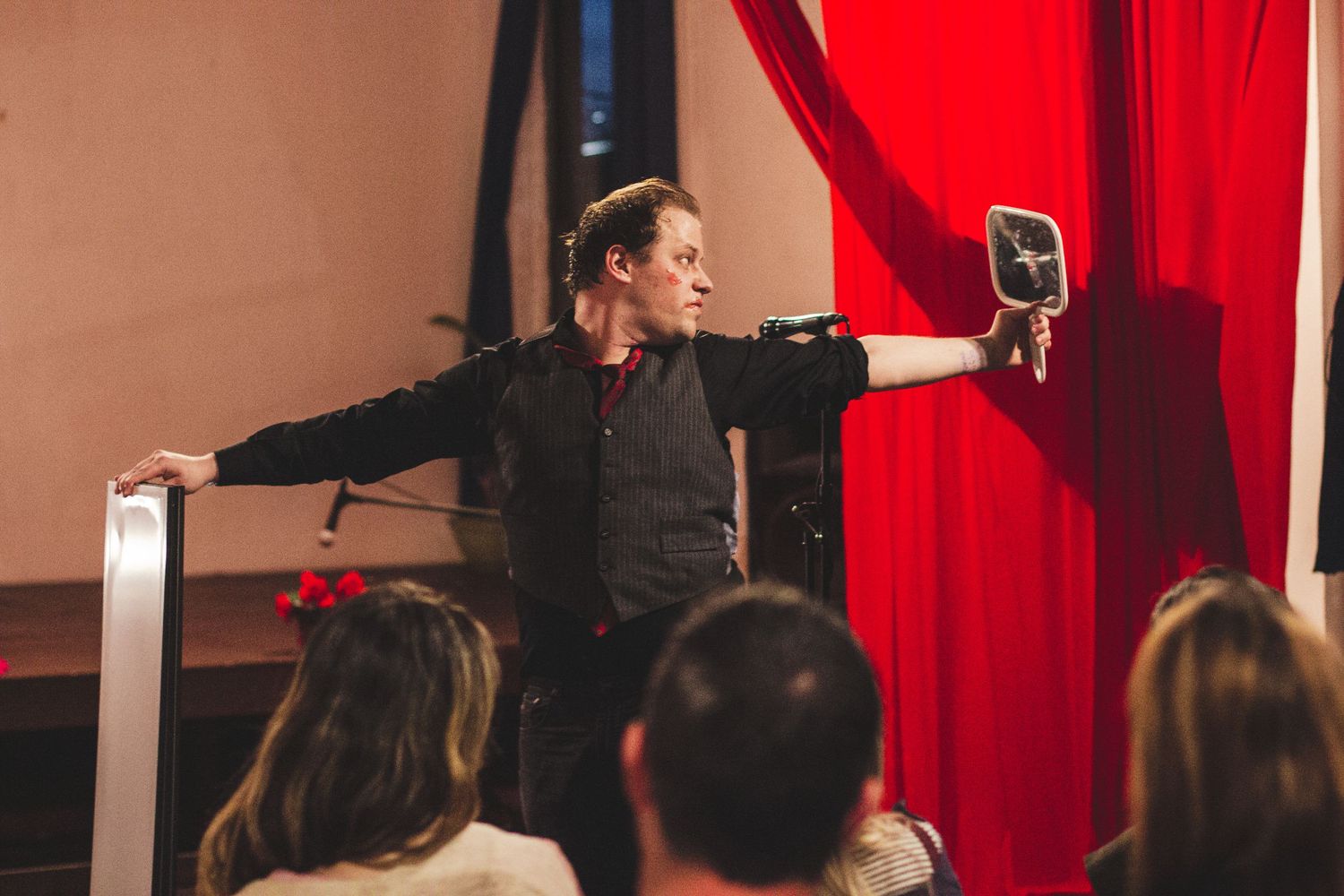 Theater audience watches performance in front of red velvet curtains.