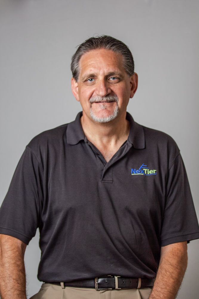 Professional headshot of person wearing a dark polo shirt with company logo against light gray background.
