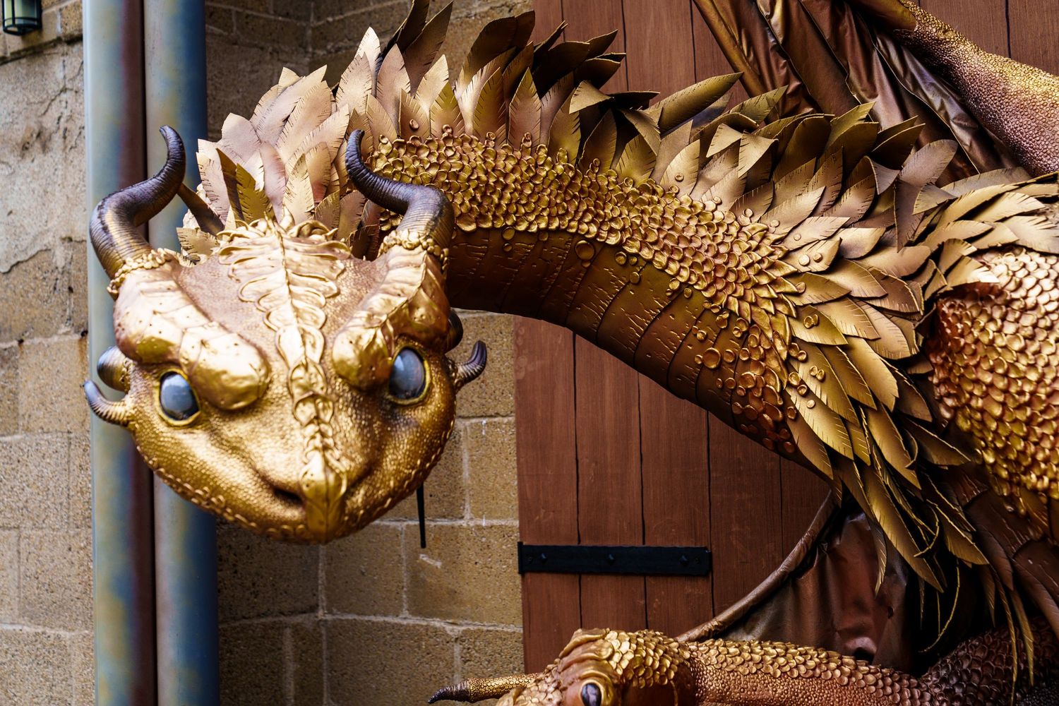 Golden dragon sculpture with intricate metalwork details mounted on a stone wall with columns.