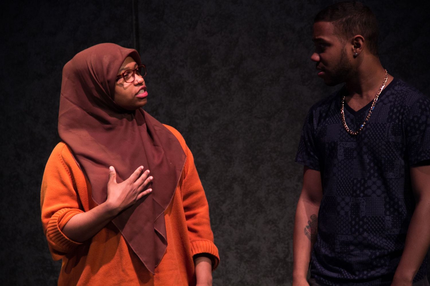 Students performing emotional scene under dramatic lighting on dark stage.