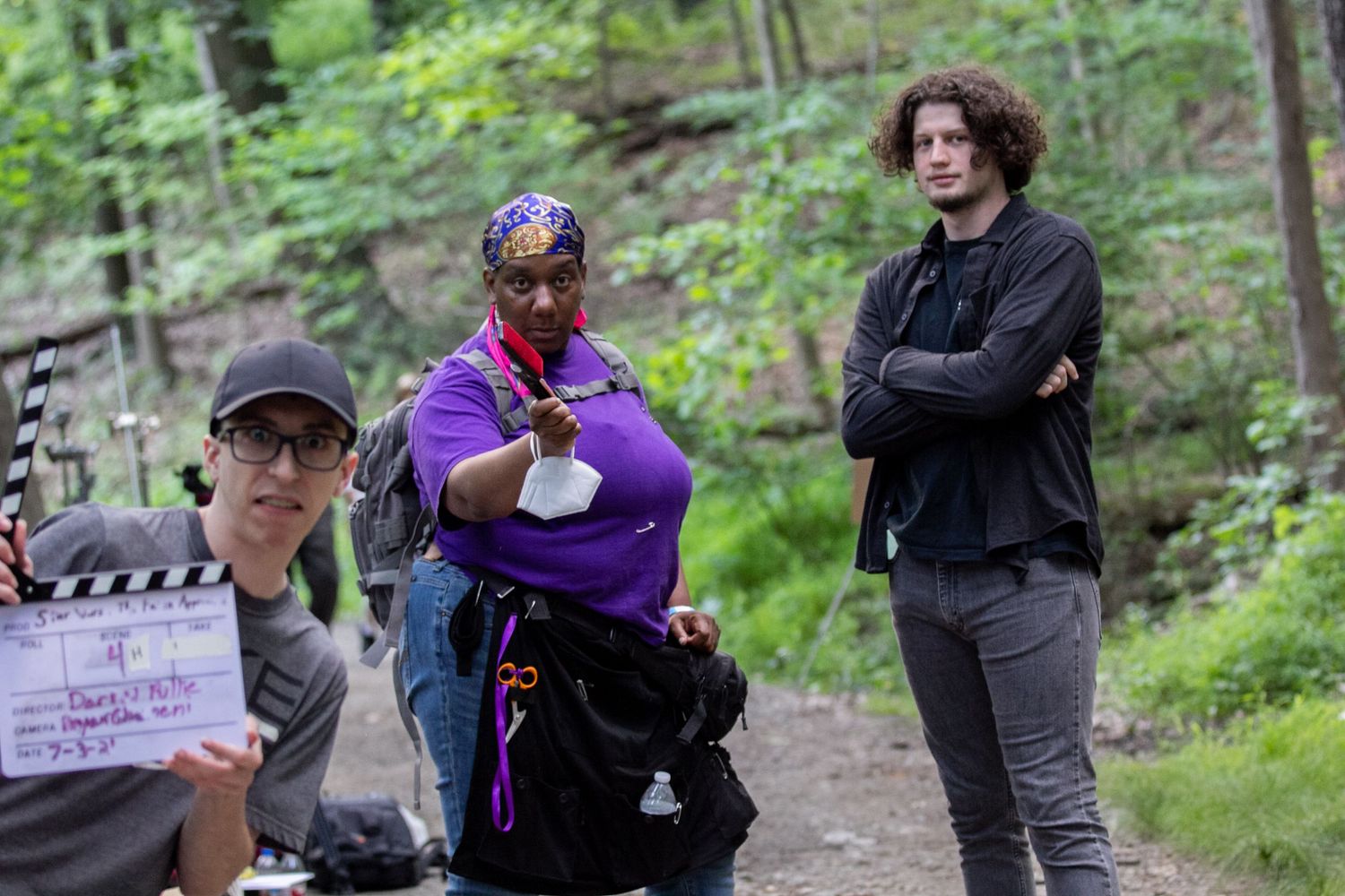 Film crew on location in woods with clapperboard, director, and talent preparing for a scene.