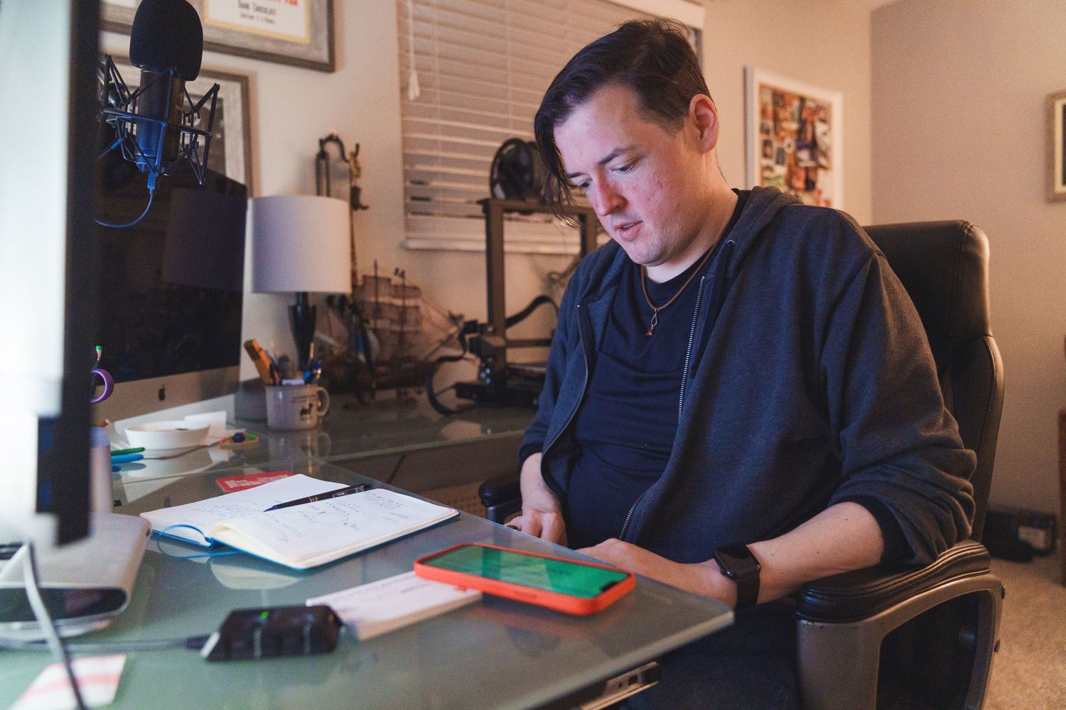 Man in navy sweater working at desk with iMac computer and tablet in home office setup.