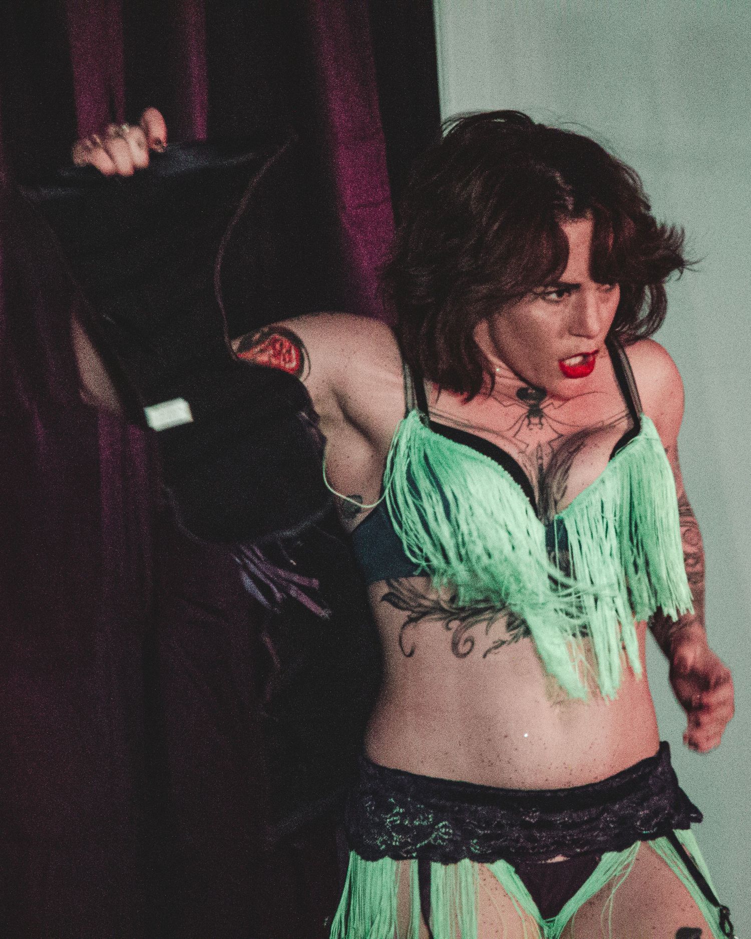 Burlesque performance featuring green fringe costume details on dark stage.