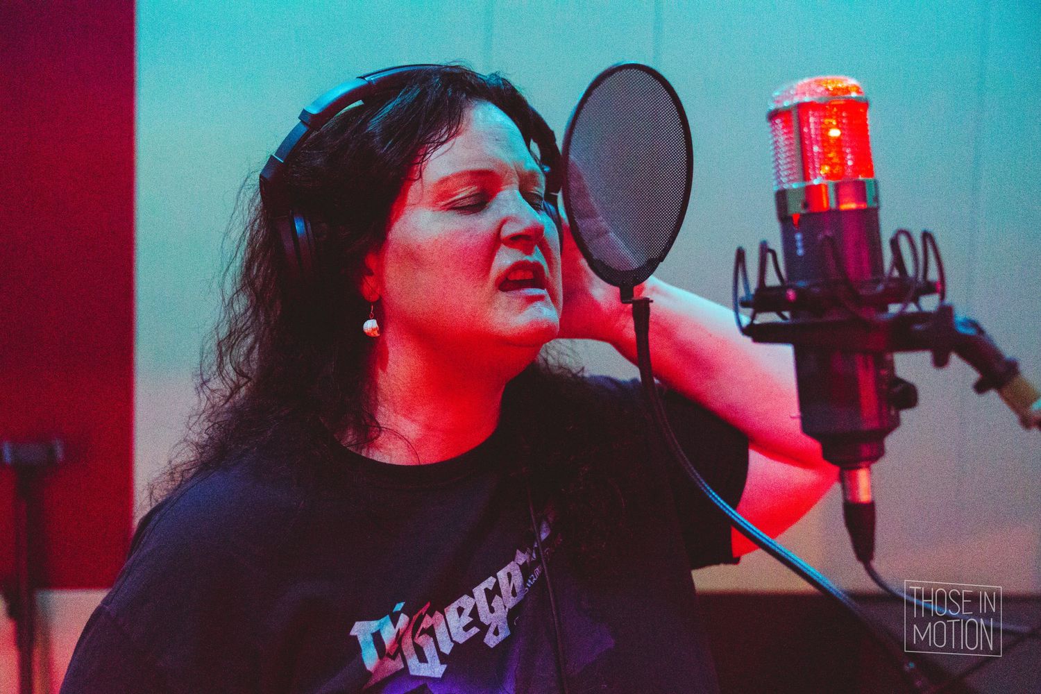 Singer performs in a recording studio booth illuminated by dramatic red and blue lighting during a vocal session.
