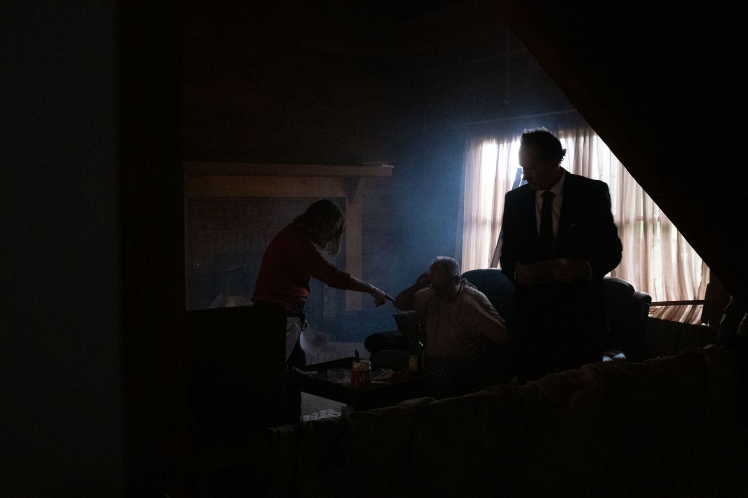 Silhouetted figures in a dimly lit room with dramatic backlight streaming through a window.