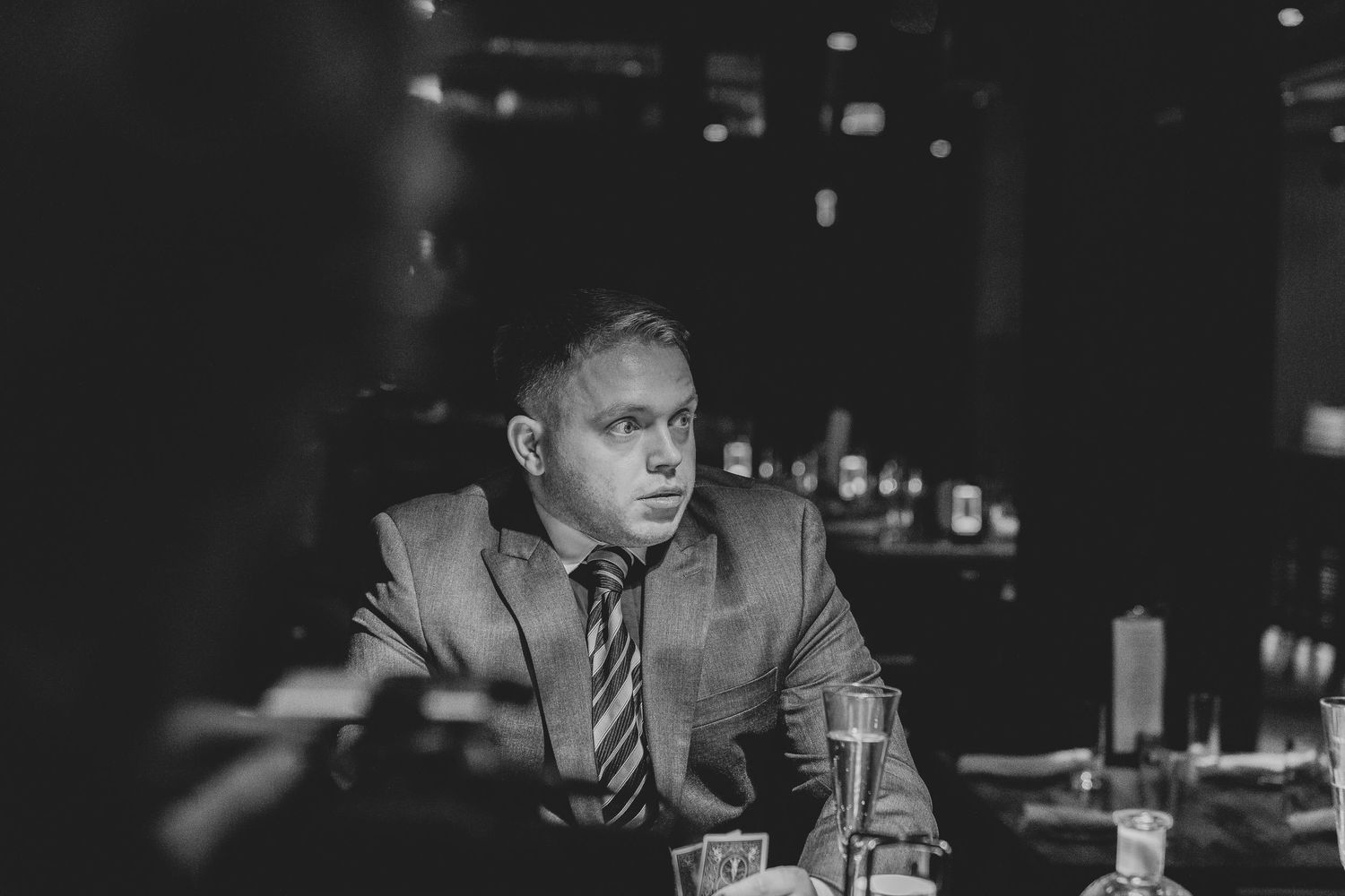 Black and white shot of bartenders working at a busy cocktail bar with bottles and glassware.