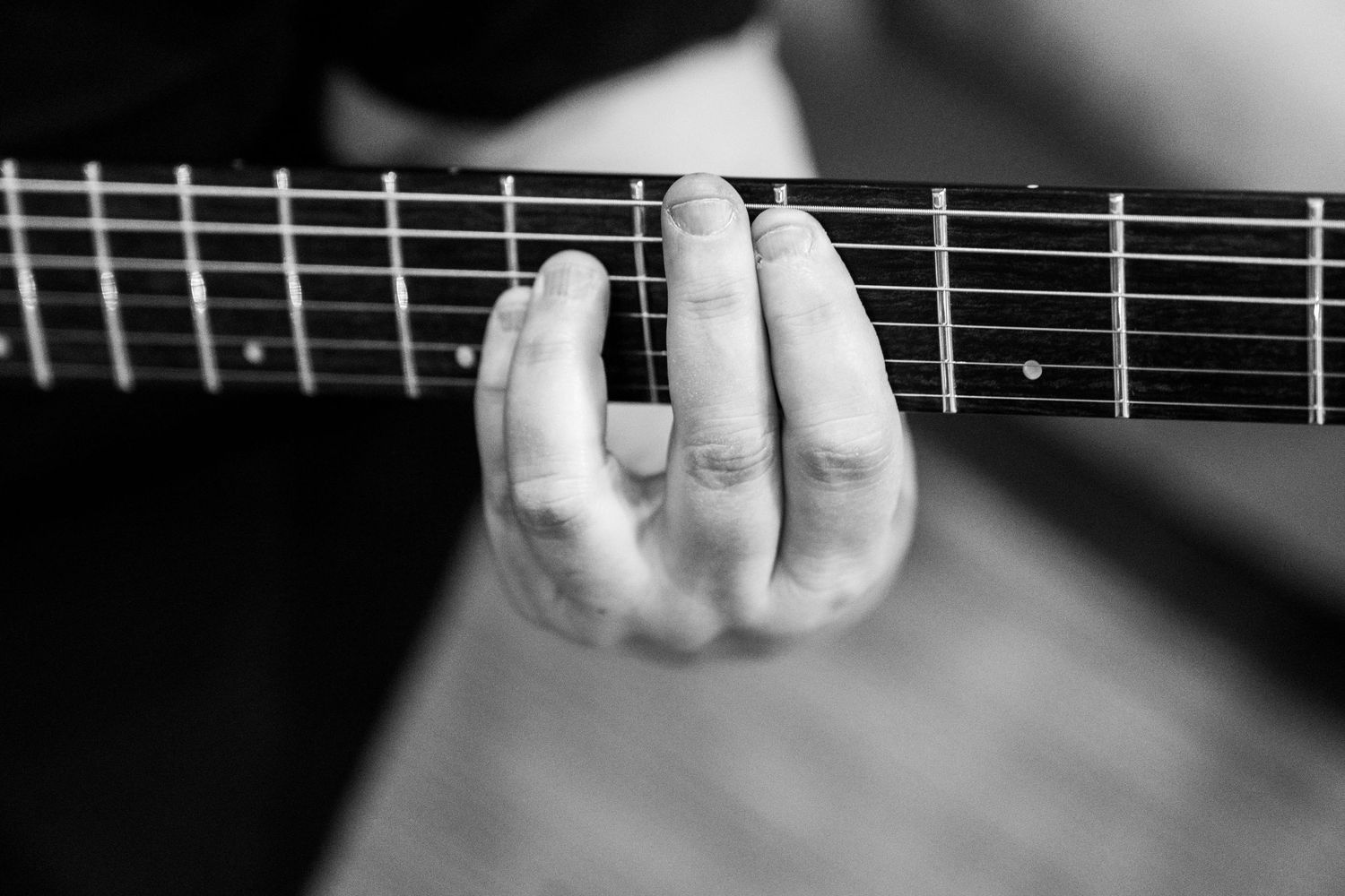 Close-up view of fingers pressing down on guitar strings against fretboard in black and white.
