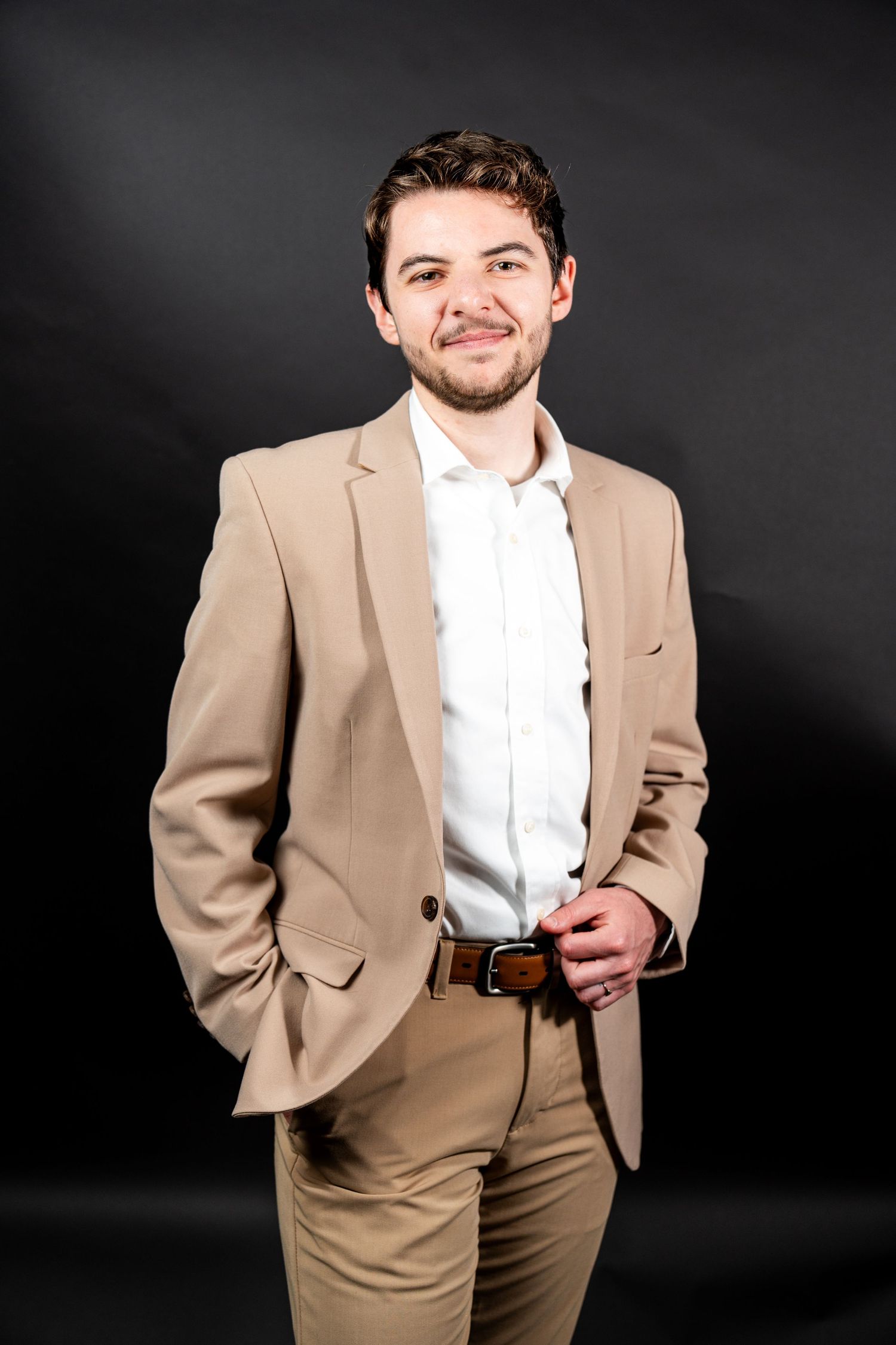 Professional portrait against dark background wearing tan suit and white dress shirt with dramatic lighting effects.