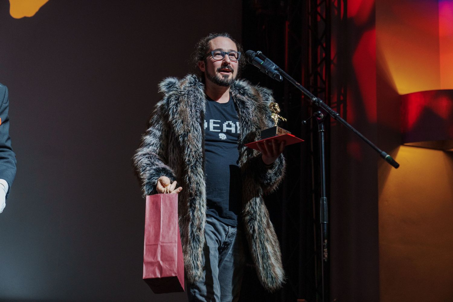 Performer in dark jacket on stage with orange ambient lighting.