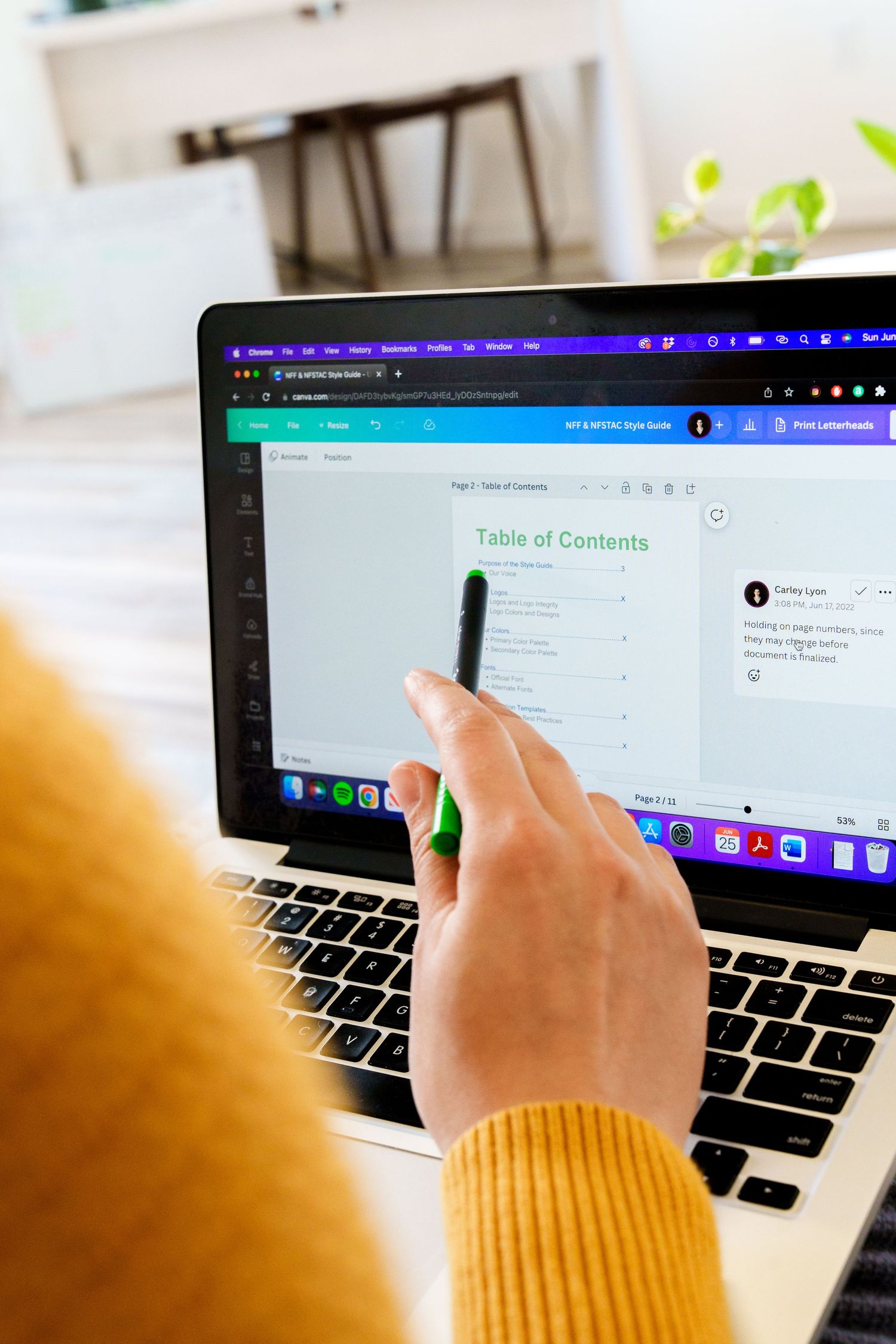 Hand pointing at table of contents on laptop screen with yellow sleeve visible.