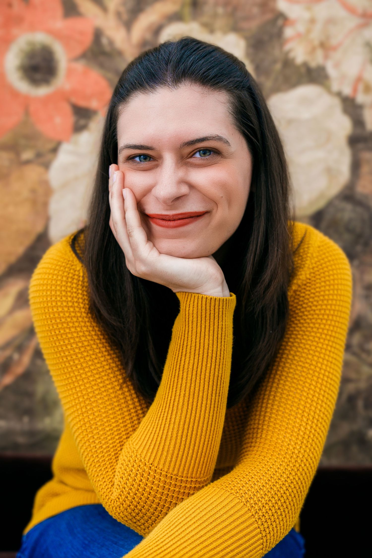 Artistic portrait against floral wallpaper featuring yellow sweater and natural pose.