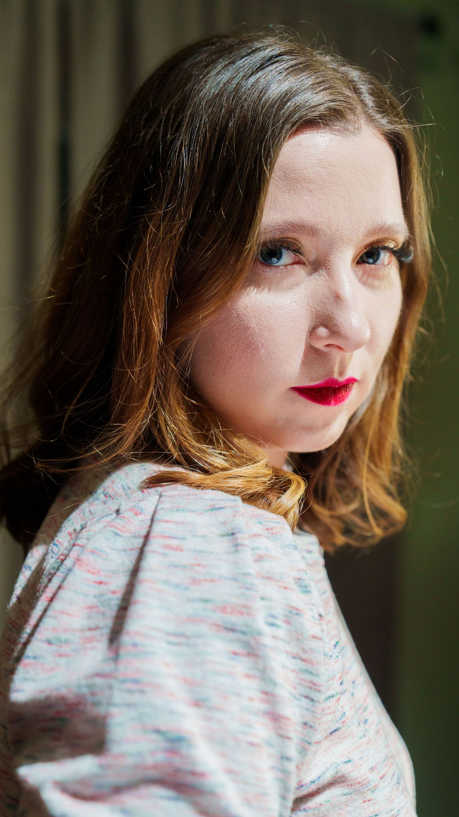 Profile views of someone wearing a white and pink patterned shirt with red lipstick against a dark background.